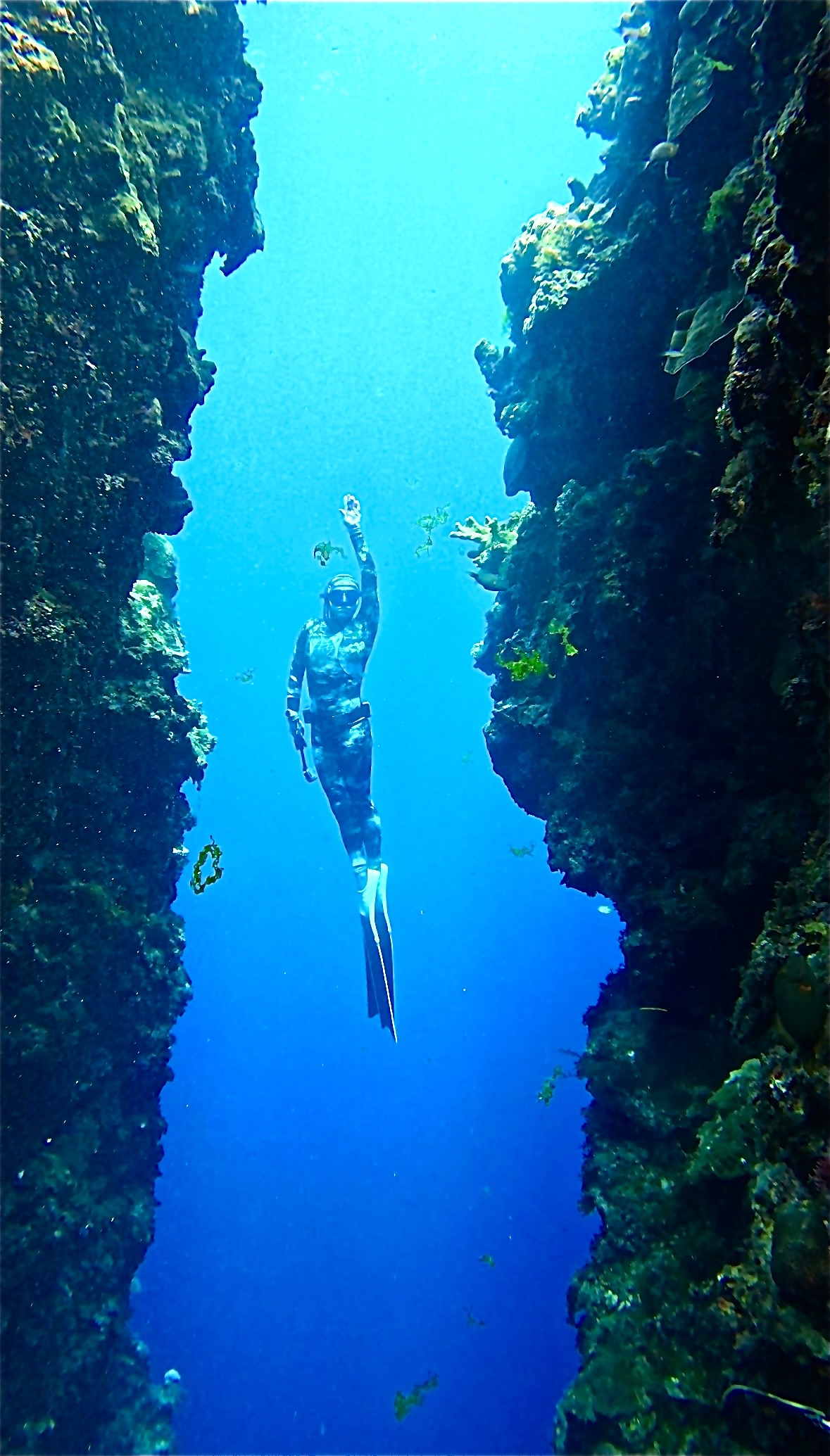 Freediver descending between two rock walls with one arm raised